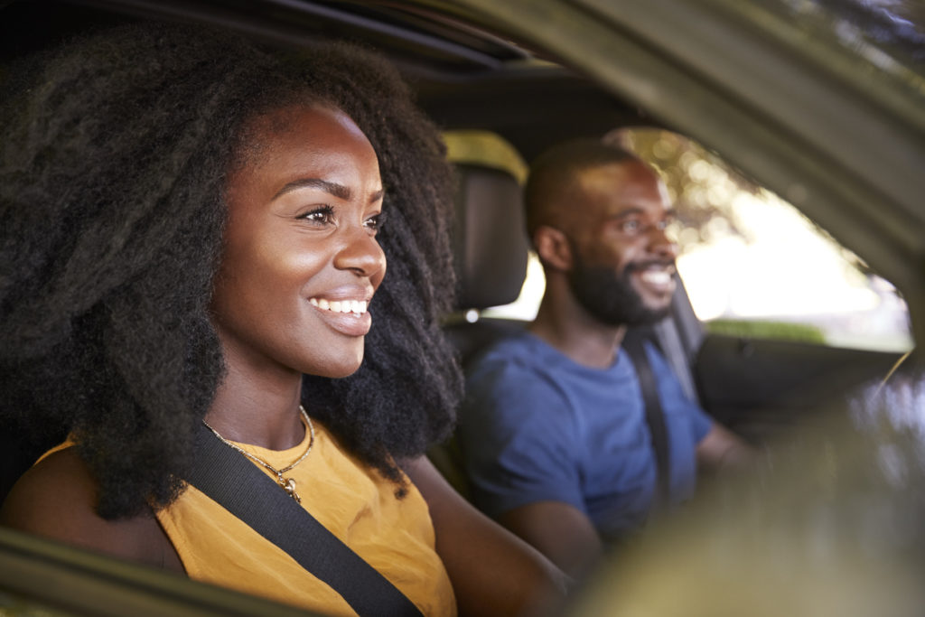 Joven pareja negra sonriendo en auto mientras viaja